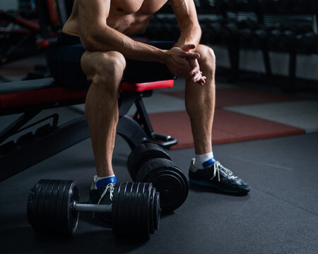 Faceless shirtless man sitting on a bench and resting after a workout. 