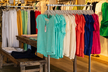 Colorful t-shirts, hanging on a rack inside a women's clothing store.