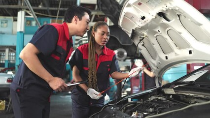 Engineer team checking under car condition on lifter in garage.Young auto mechanic in uniform is looking at camera and smiling examining car.
