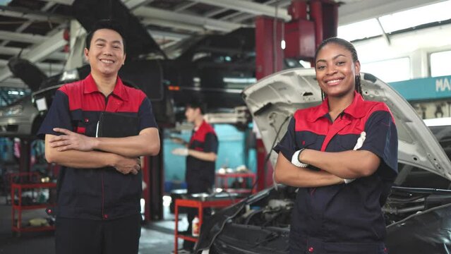 Engineer team checking under car condition on lifter in garage.Young auto mechanic in uniform is looking at camera and smiling examining car.