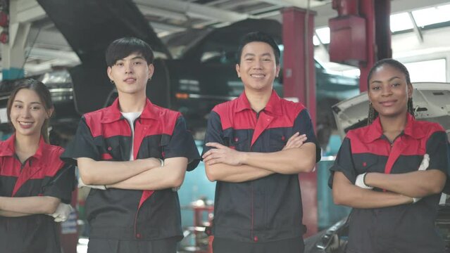 Engineer team checking under car condition on lifter in garage.Young auto mechanic in uniform is looking at camera and smiling examining car.