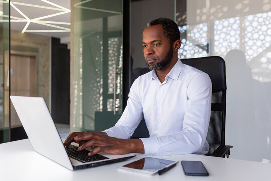 Serious focused african american programmer working inside office, man coding new software on laptop, mature experienced team leader developing technical project. - Powered by Adobe