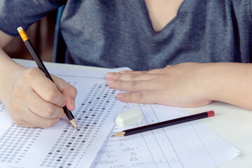 Students hand holding pencil writing selected choice on answer sheets and Mathematics question sheets. students testing doing examination. school exam