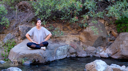 Young woman meditating outdoor by the riverside. Yoga exercising in nature. Drone aerial photo