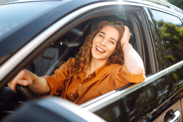 Smiling woman driving a car. Attractive woman sitting in the driver's seat of a car. Outdoor portrait. The concept of transport, lifestyle.