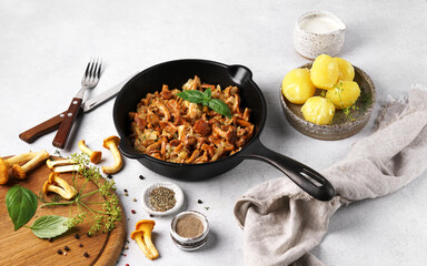 Cooked chanterelle mushrooms with onions and spices in a pan on the kitchen table grnished with potatoes.