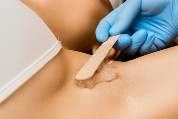 Professional smears transparent wax on lady client armpit area. Hair removal and spa services. Smearing stretchy structure on woman body part