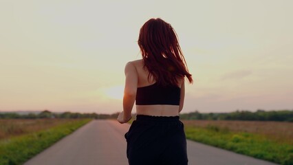 Jogger girl breathes fresh air in nature. Running after sun. Training jogging. Beautiful girl doing fitness, jogging on road in sun. Free young woman runs in summer park, sunset. Jogging outside city