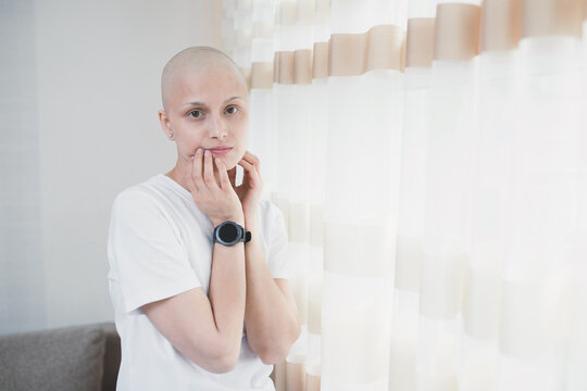 Calm young woman with leukemia after chemotherapy stands alone in the room.