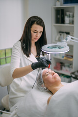 Cosmetologist and dermatologist makes injections with a mesotherapy apparatus to a lying woman patient in a beauty salon.