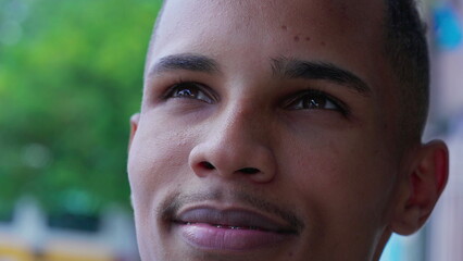 Fototapeta premium One black Brazilian young man gazing upwards at sky with HOPE and FAITH. Contemplative South American male person with happy expression, looking up close-up face