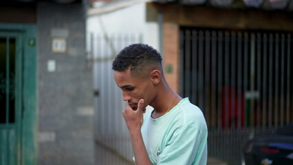 One pensive young black Brazilian man concerned about life while walking in urban street. Anxious African American descent person strolling in urban environment rubbing face and neck