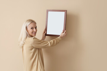 Mature woman hanging blank frame on beige wall