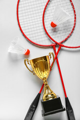 Gold cup with badminton rackets and shuttlecocks on light background