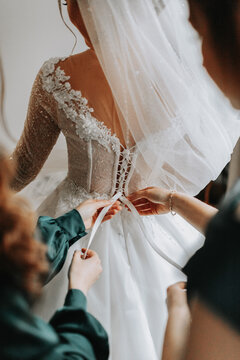 Close-up photo of a beautiful bride from the back, bridesmaids helping to tie the wedding dress