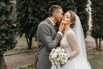 Stylish bride and groom tenderly embrace and kiss. Beautiful bride with modern bouquet embracing stylish groom in autumn park. Sensual romantic moment. Wedding. Stylish and beautiful.
