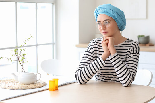 Young woman after chemotherapy sitting at table in kitchen