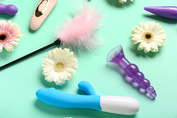 Sex toys with flowers on mint background, closeup