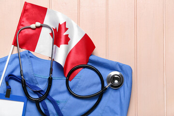 Canadian flag with doctor's uniform, badge and stethoscope on beige wooden background, closeup