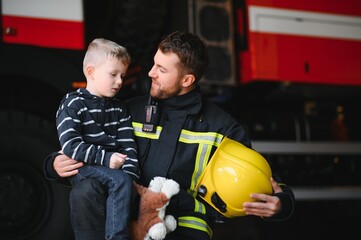 A firefighter take a little child boy to save him. Fire engine car on background. Fireman with kid...
