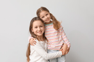 Cute little sisters hugging on light background