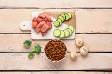 Composition with dry pet food, raw meat and natural products on light wooden background
