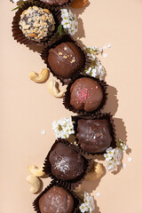 Chocolate craft nuts candies on white plate on beige background flat lay, top view