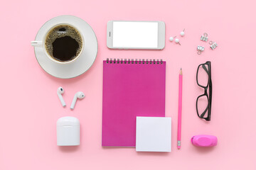 Cup of coffee with eyeglasses, gadgets and stationery on pink background