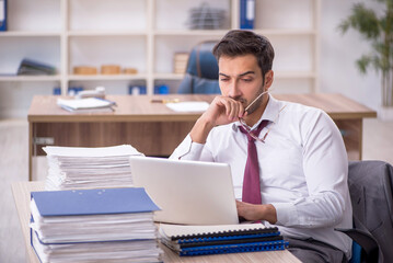 Obraz premium Young male employee and too much work at workplace