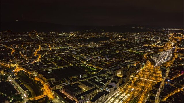 Aerial hyperlapse footage of night city. Fly above train station and buildings in surrounding urban boroughs. Zurich, Switzerland