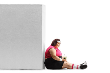 Unhappy overweight woman in sportswear holding a healthy green shake and sitting on the ground