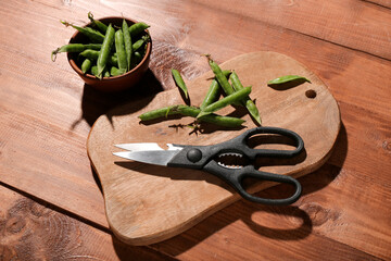 New cutting board, scissors and bowl with green peas on wooden background