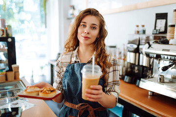 Young coffee shop worker holding takeaway drinks and desserts. Business concept, food to go, small business.