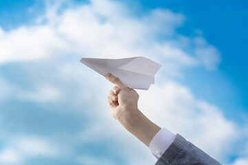 paper white origami airplane in a male hand against a blue sky, a start in business, a symbol of travel and freedom