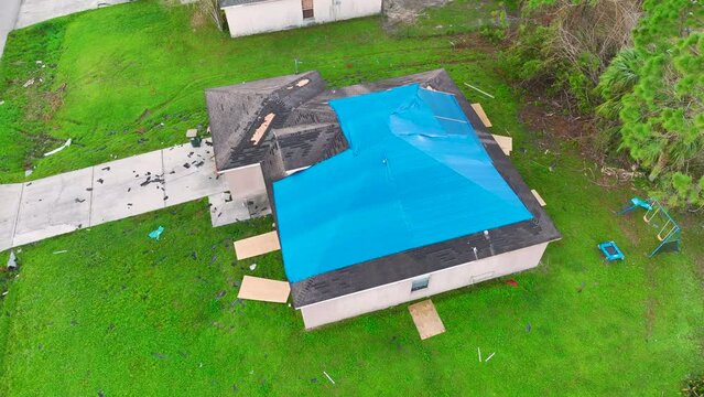 Top view of leaking house roof covered with protective tarp sheets against rain water leaks until replacement of asphalt shingles. Damage of building rooftop as aftermath of hurricane Ian in Florida