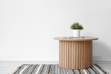 Wooden coffee table with houseplant and magazines near white wall