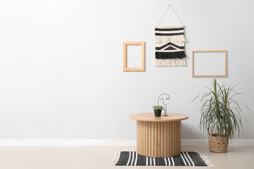 Wooden coffee table and houseplant near grey wall with macrame