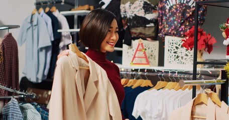 Woman browsing through elegant blazers on racks in Christmas decorated shopping store, looking for perfect xmas dinner attire. Fashionable customer in need of new clothes