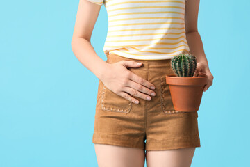 Young woman with cactus suffering from cystitis on blue background, closeup
