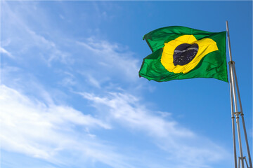 Uma bandeira do Brasil balançando ao vento com o céu azul ao fundo.
