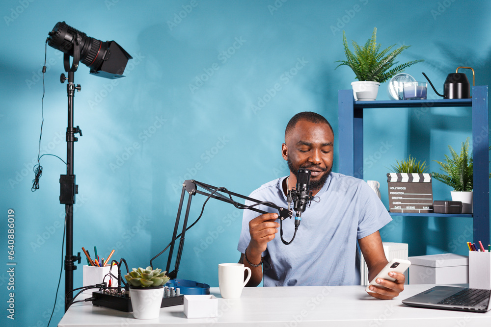 Poster smiling blogger reading subscribers questions on smartphone while recording video. cheerful african 