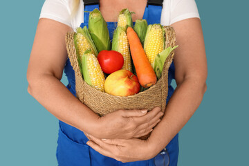 Mature female farmer with wicker basket full of different ripe vegetables on blue background