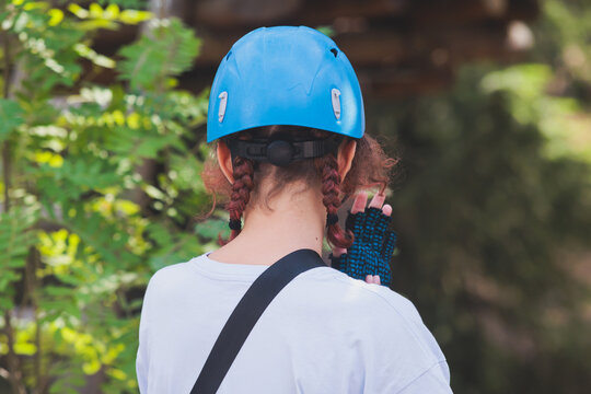 View of high ropes course, kids of climbing in amusement acitivity rope park, passing obstacles and zip line on heights, children teenagers in equipment gear between the trees on heights, summer day