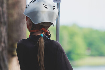 View of high ropes course, kids of climbing in amusement acitivity rope park, passing obstacles and zip line on heights, children teenagers in equipment gear between the trees on heights, summer day