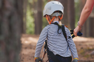 View of high ropes course, kids of climbing in amusement acitivity rope park, passing obstacles and zip line on heights, children teenagers in equipment gear between the trees on heights, summer day