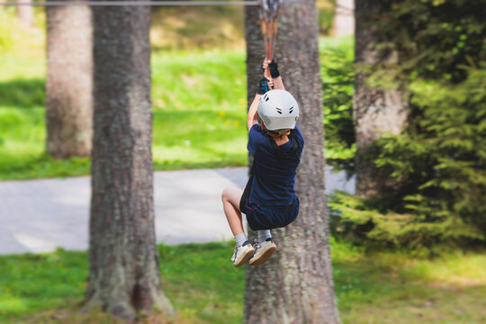 View of high ropes course, kids of climbing in amusement acitivity rope park, passing obstacles and zip line on heights, children teenagers in equipment gear between the trees on heights, summer day