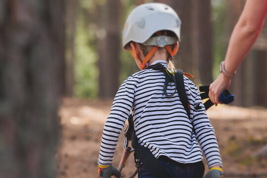 View of high ropes course, kids of climbing in amusement acitivity rope park, passing obstacles and zip line on heights, children teenagers in equipment gear between the trees on heights, summer day