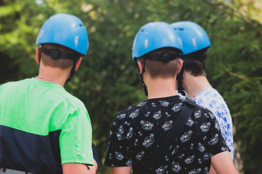 View of high ropes course, kids of climbing in amusement acitivity rope park, passing obstacles and zip line on heights, children teenagers in equipment gear between the trees on heights, summer day