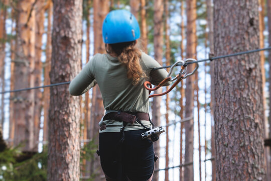 View of high ropes course, kids of climbing in amusement acitivity rope park, passing obstacles and zip line on heights, children teenagers in equipment gear between the trees on heights, summer day