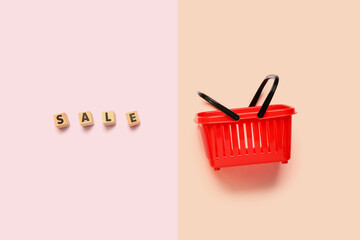 Fototapeta premium Small red shopping basket with text SALE on color background